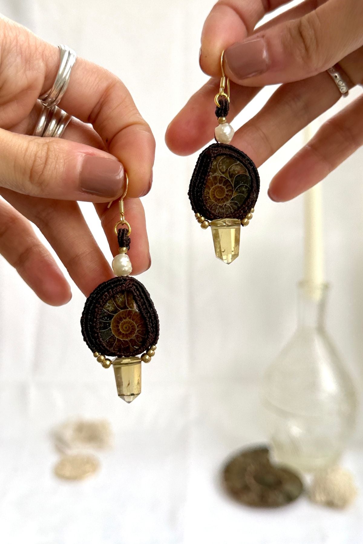 Sliced ammonite and smoky quartz earrings shown in hand, highlighting freshwater pearls and fluid motion