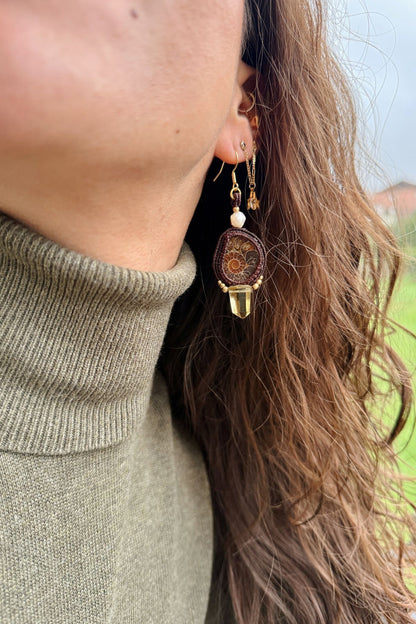 Detailed view of sliced ammonite earrings on model, showing pearl and smoky quartz point, movement and lightweight design