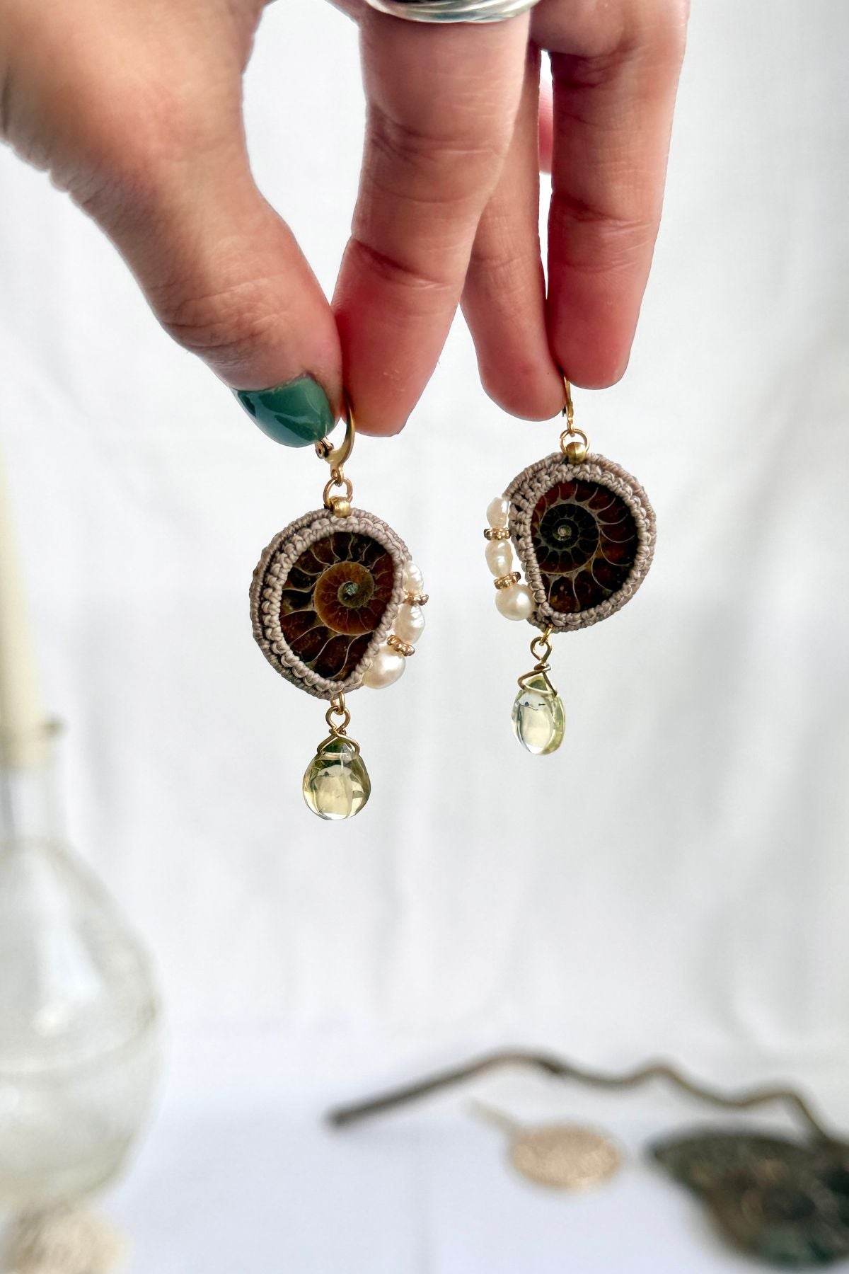 Hand holding ammonite fossil and pearl hoop earrings with lemon quartz drops showing scale and natural details