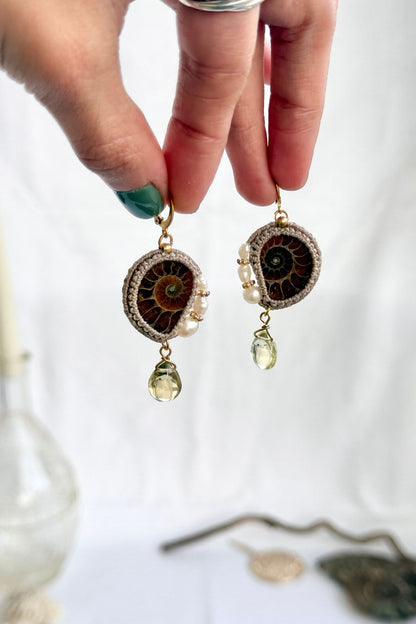 Hand holding ammonite fossil and pearl hoop earrings with lemon quartz drops showing scale and natural details