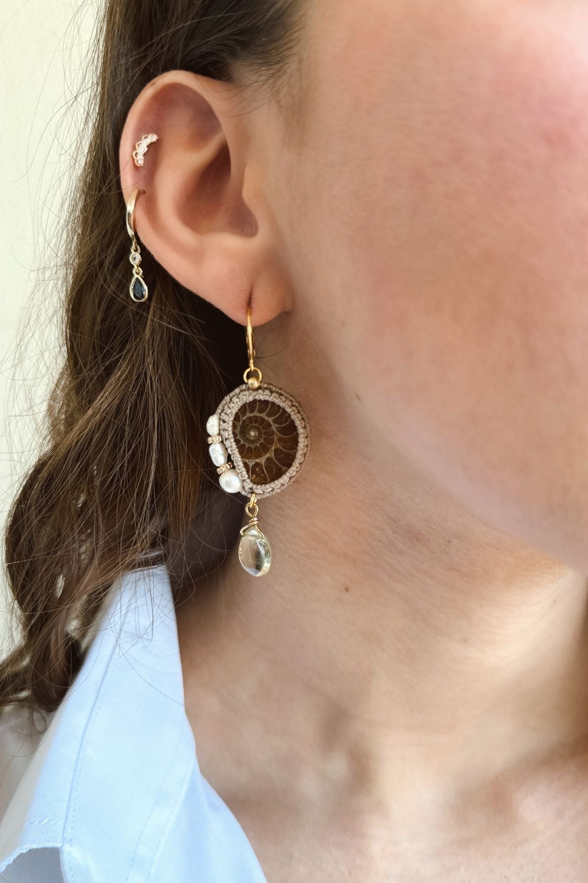 Close-up of ammonite fossil hoop earrings on model highlighting freshwater pearls and lemon quartz movement