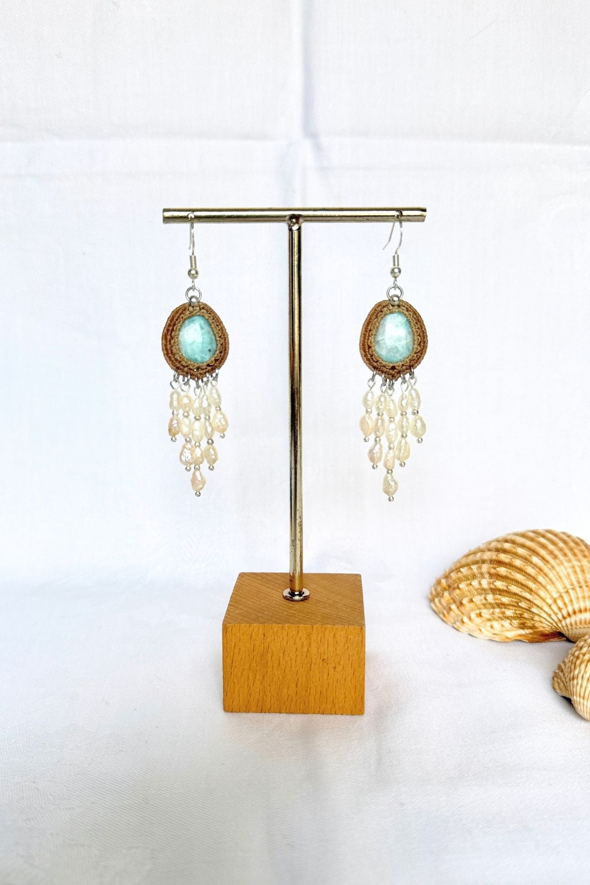 Handmade Larimar and freshwater pearl dangle earrings on a stand beside decorative shells.