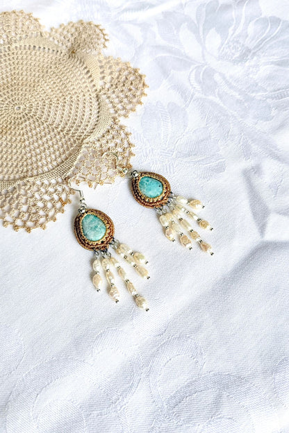 Pair of Larimar macrame earrings with freshwater pearl strands laid on white fabric beside crochet lace.