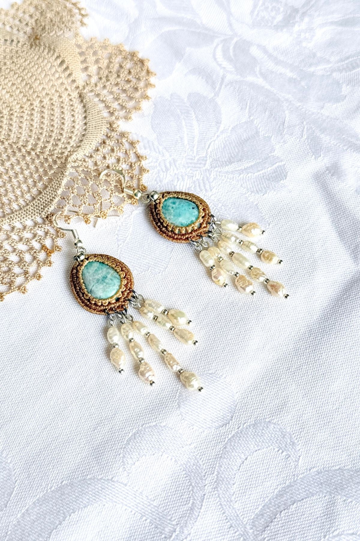 Close-up of Larimar stones framed in beige macrame with cascading freshwater pearls on white fabric.