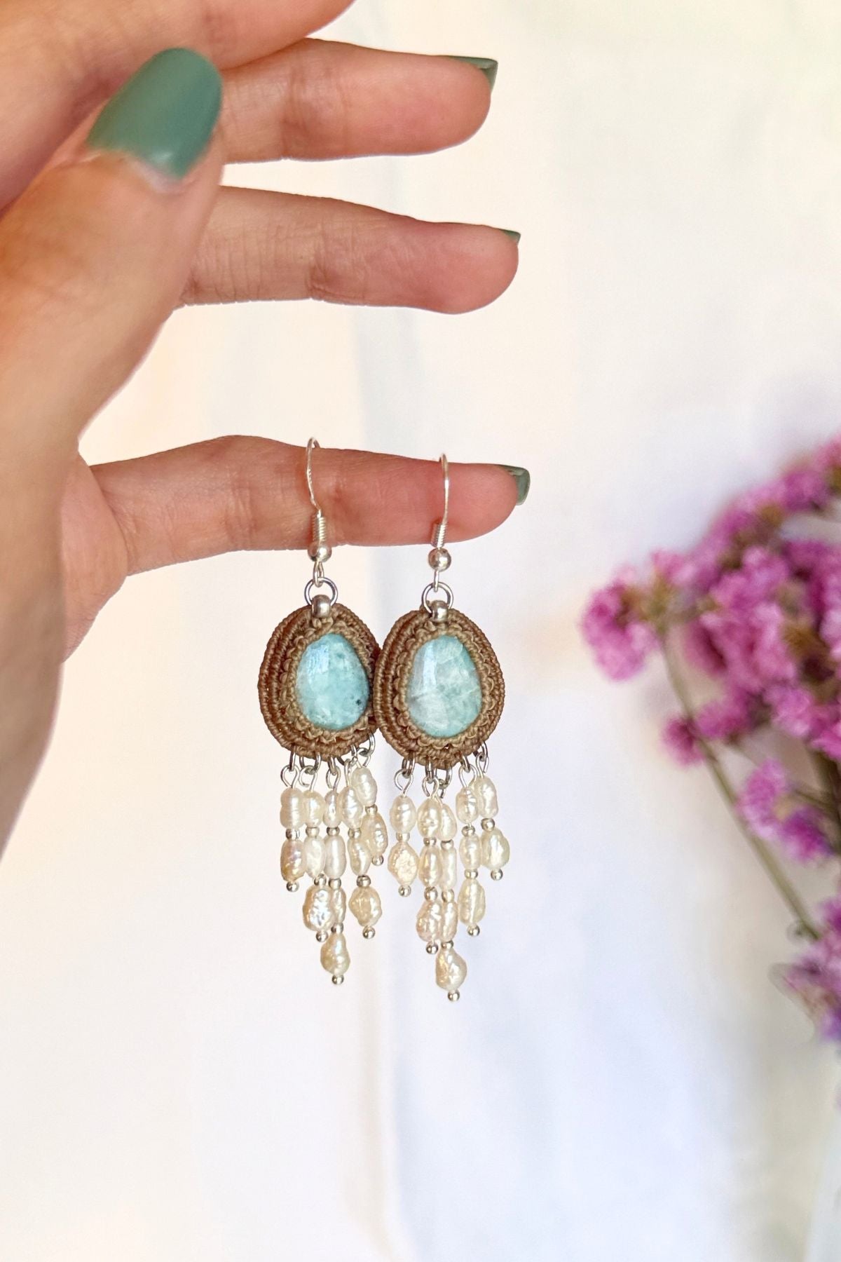Hand holding a pair of handmade Larimar macrame earrings with freshwater pearl cascades.