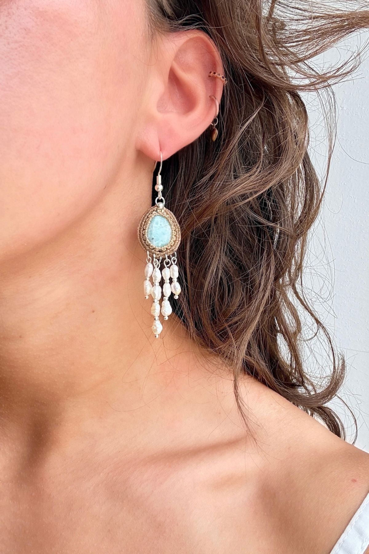Close-up of a Larimar macrame earring with freshwater pearl strands worn on the ear.
