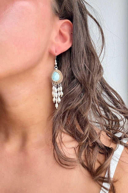 Larimar and freshwater pearl dangle earring worn on the ear, showing its length beside the neck.