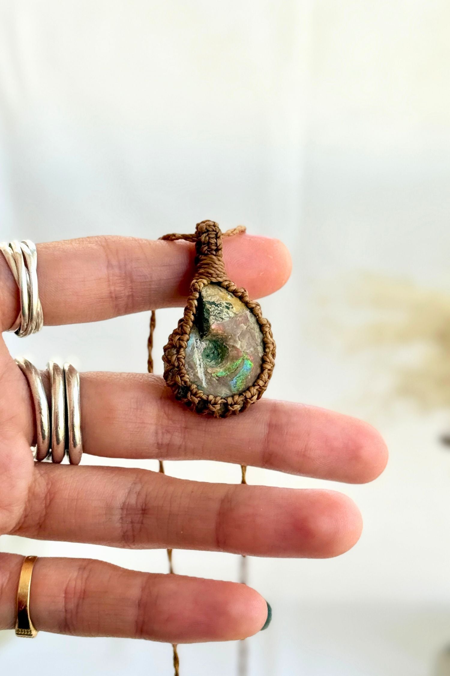 Hand holding a handmade Ammonite Macrame necklace from the Essence collection, featuring a high-quality gemstone in a delicate everyday-wear design.