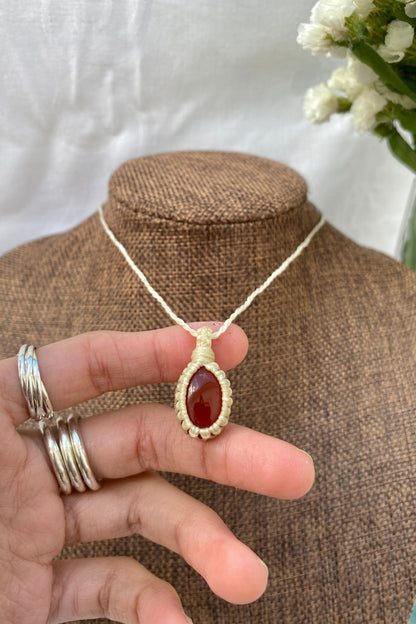 Close-up of a handmade Carnelian macrame necklace on a display stand, with a hand holding the piece to showcase its fine details and craftsmanship.