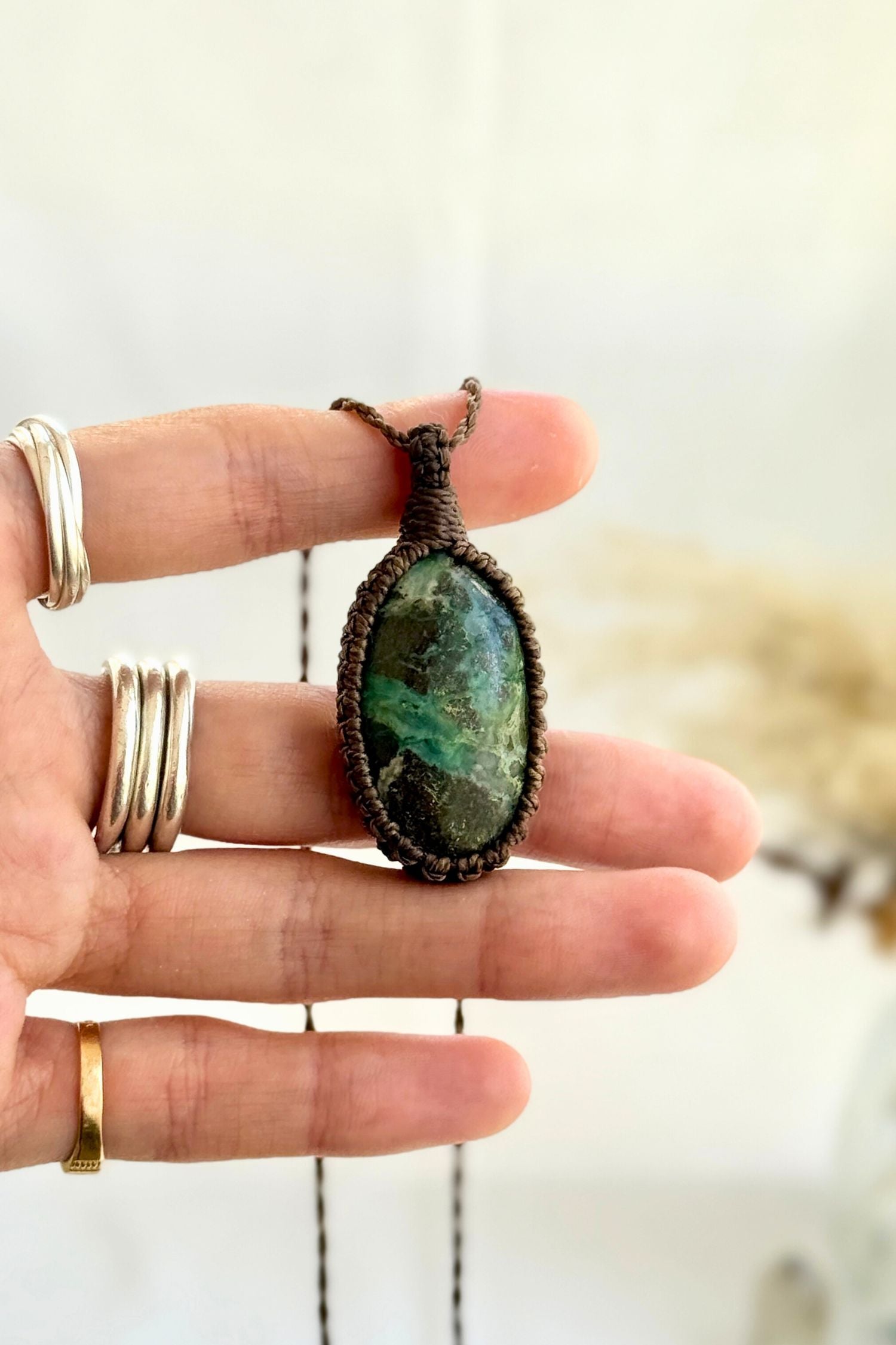 Hand holding a handmade Chrysocolla Macrame necklace from the Essence collection, featuring a high-quality gemstone in a delicate everyday-wear design.