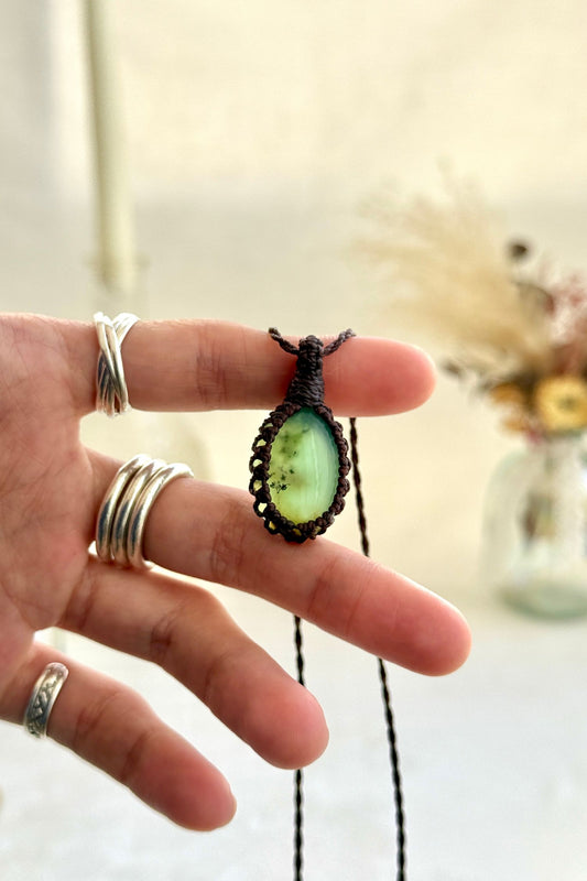 Hand holding a handmade Chrysoprase macrame necklace with a brown cord, showcasing the gemstone's vibrant green, semi-translucent color.