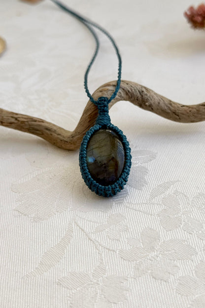 Handmade Labradorite macrame necklace with a blue cord, laid flat to display its intricate design and glowing gemstone.