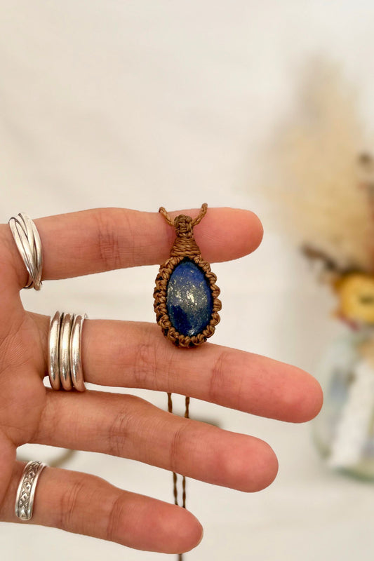 Hand holding a handmade Lapis Lazuli macrame necklace with a camel brown cord, showcasing the gemstone's mysterious beauty, revealing magical golden pyrite inclusions.