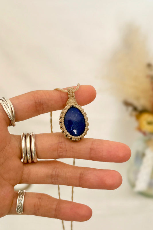 Hand holding a handmade Lapis Lazuli macrame necklace with a beige cord, showcasing the gemstone's mysterious beauty, revealing magical golden pyrite inclusions.