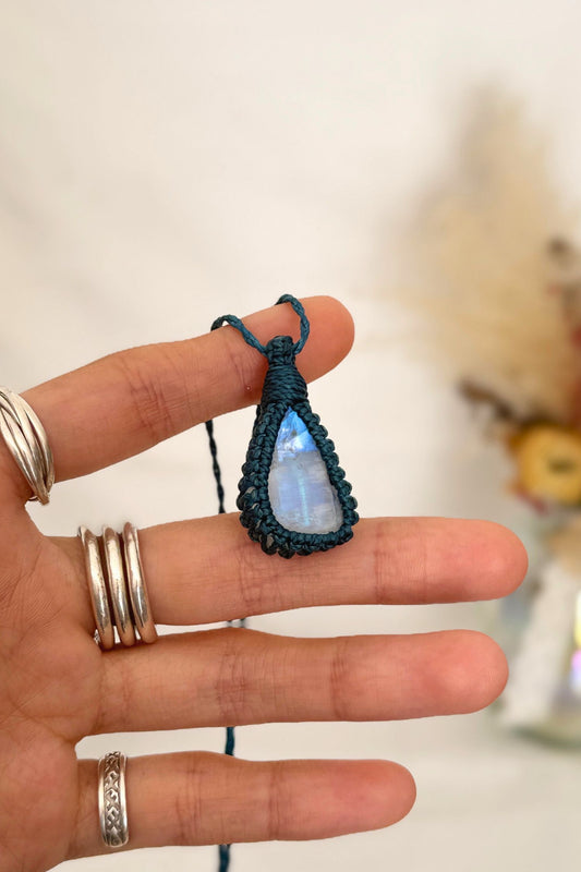 Hand holding a handmade Rainbow Moonstone macrame necklace with a blue cord, showcasing the gemstone's mysterious beauty, revealing magical rainbow flashes.