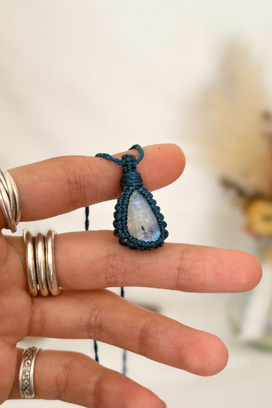 Hand holding a handmade Rainbow Moonstone macrame necklace with a blue cord, showcasing the gemstone's mysterious beauty, revealing magical rainbow flashes.