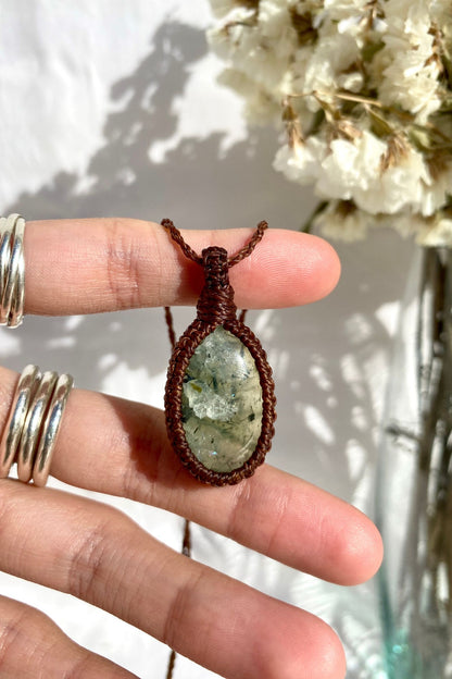 Hand holding a delicate handmade Prehnite macrame necklace, featuring a soft green gemstone with natural inclusions.