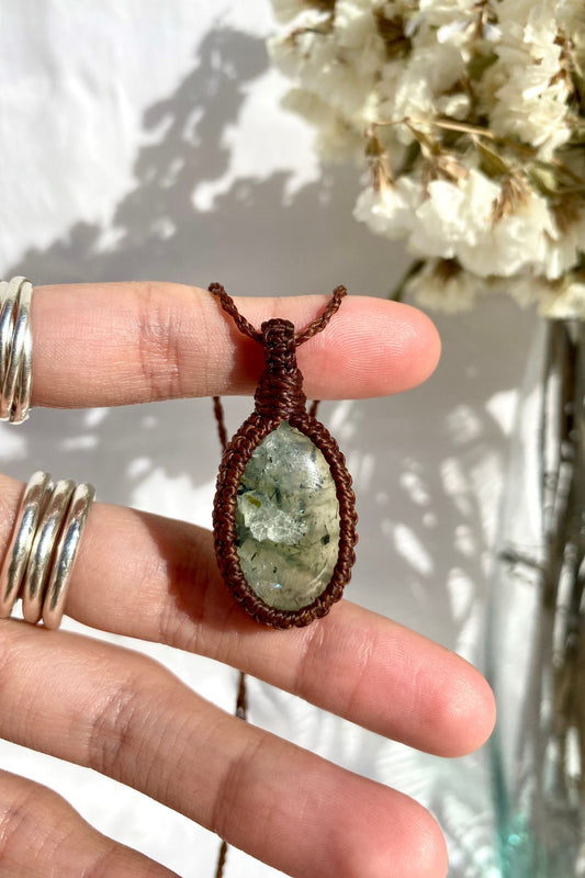Hand holding a delicate handmade Prehnite macrame necklace, featuring a soft green gemstone with natural inclusions.