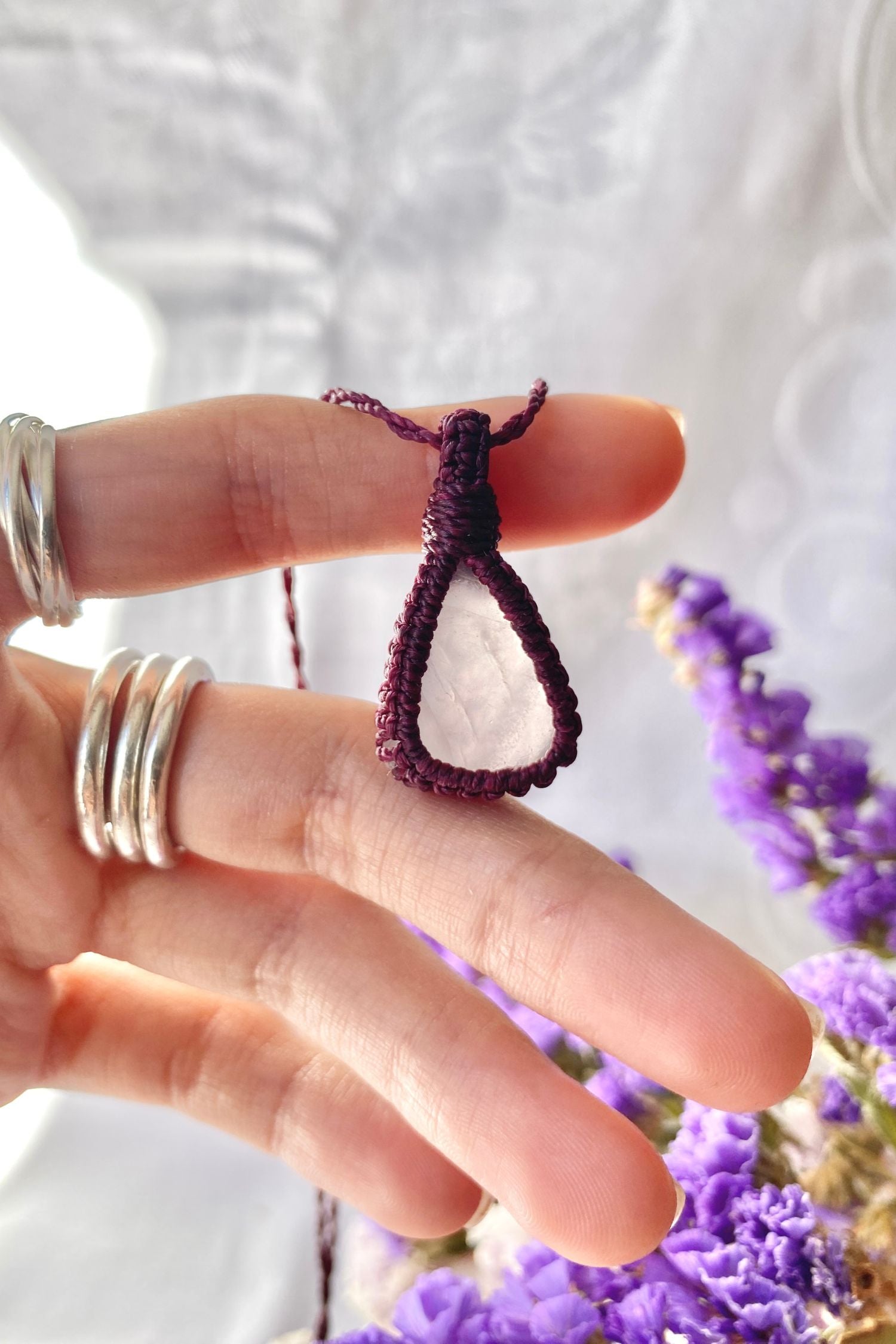 Hand holding a delicate handmade macrame necklace featuring a soft pink rose quartz gemstone wrapped in burgundy macrame cord.