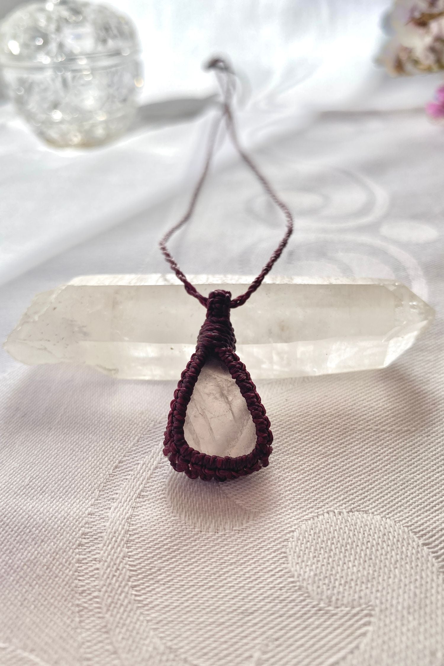 Handmade rose quartz macrame necklace laid flat, showcasing its romantic soft pink gemstone and elegant burgundy cord design.