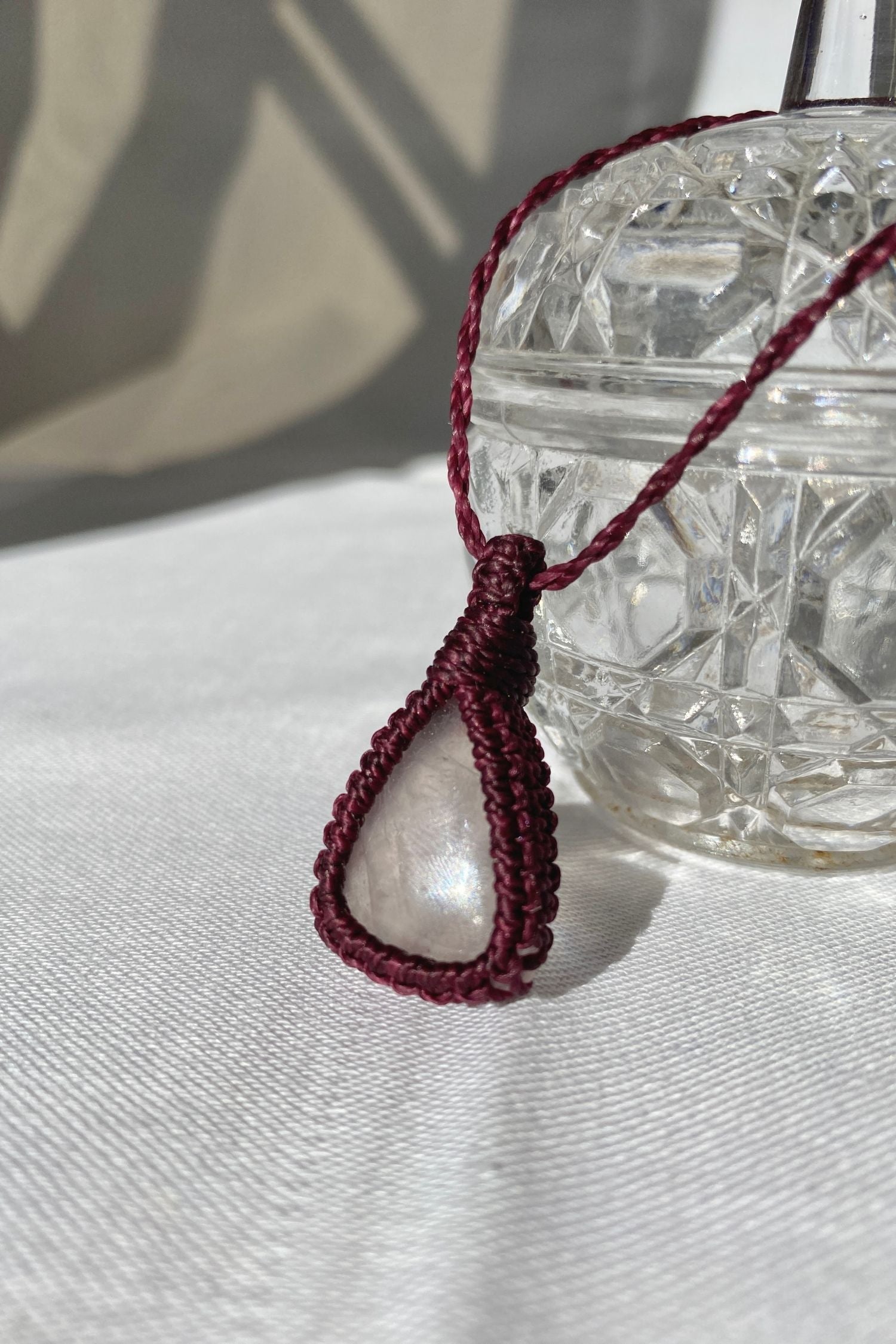 Rose quartz macrame necklace glowing in sunlight, enhancing the soft pink tones of the gemstone and the deep burgundy cord.