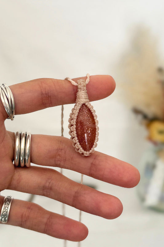 Hand holding a handmade Sunstone macrame necklace with a white cord, showcasing the gemstone's vibrant color holding a mysterious beauty, revealing a subtle shimmer.