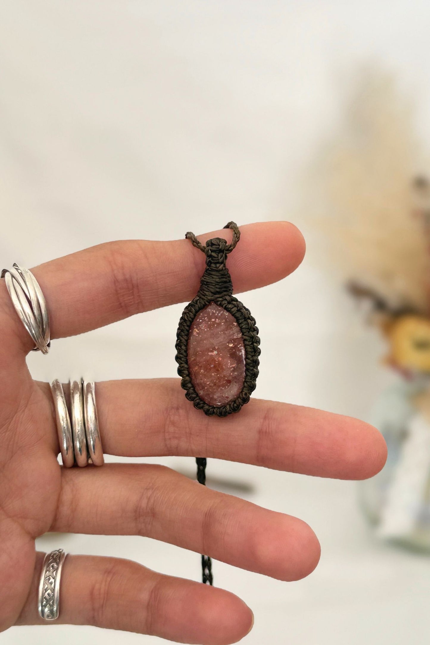 Hand holding a handmade Sunstone macrame necklace with a dark green cord, showcasing the gemstone's vibrant color holding a mysterious beauty, revealing a subtle shimmer.