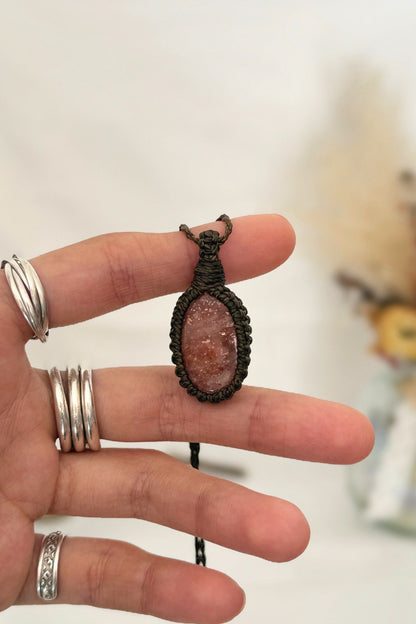 Hand holding a handmade Sunstone macrame necklace with a dark green cord, showcasing the gemstone's vibrant color holding a mysterious beauty, revealing a subtle shimmer.