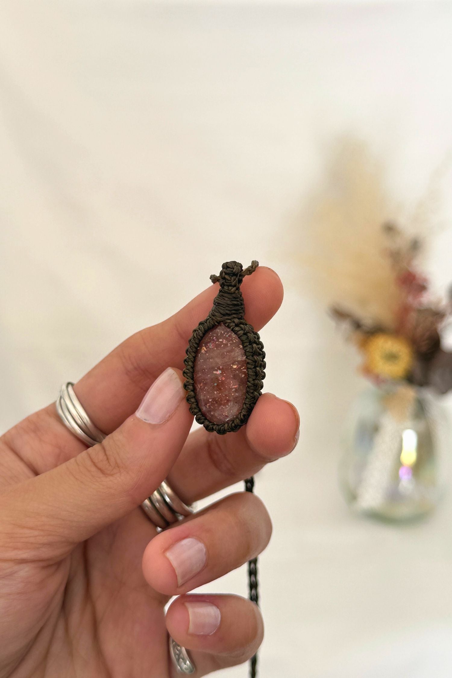 Close-up of handmade Sunstone Macrame necklace in hand, showcasing the intricate macrame knotting and the vibrant sparkly hues of the gemstone.