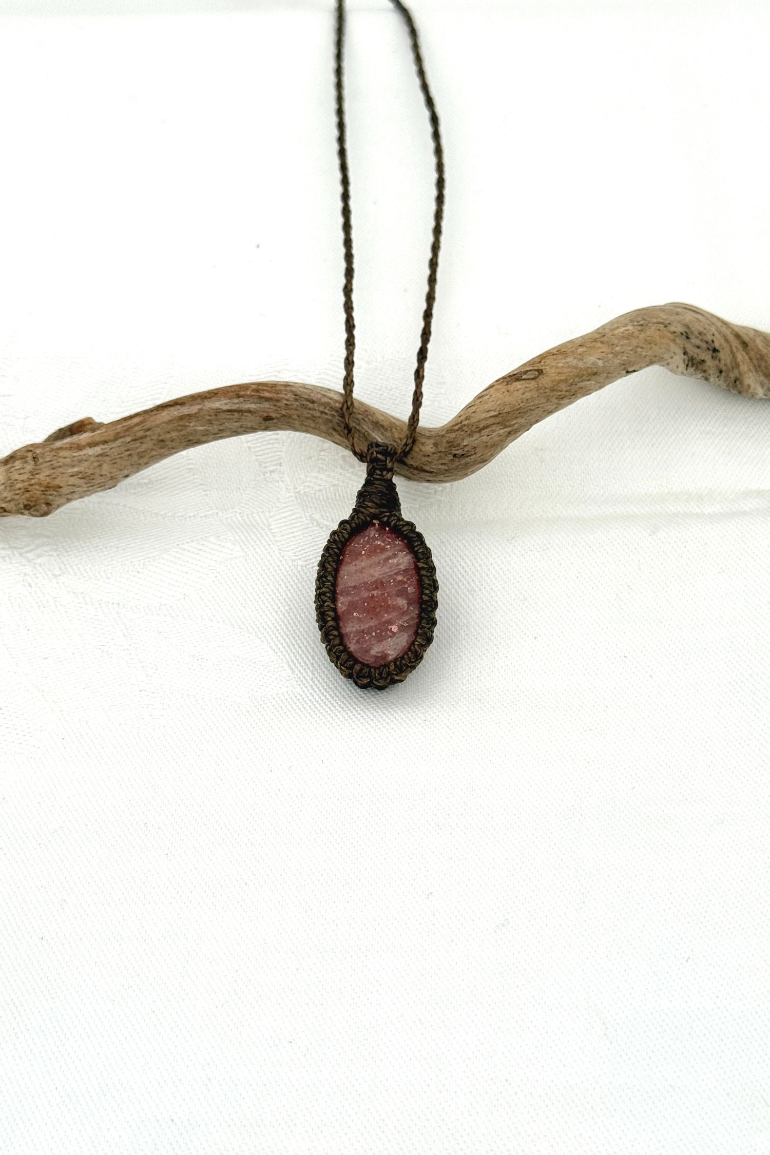 Handmade Sunstone macrame necklace with a dark green cord, laid flat to display its intricate design and glowing gemstone.