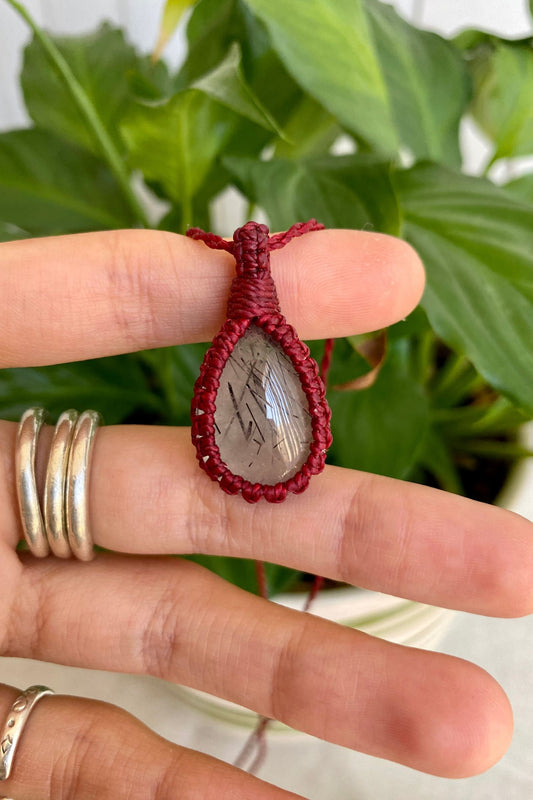 Hand holding a handmade Tourmaline Quartz macrame necklace, showcasing the gemstone’s striking black tourmaline inclusions within clear quartz.