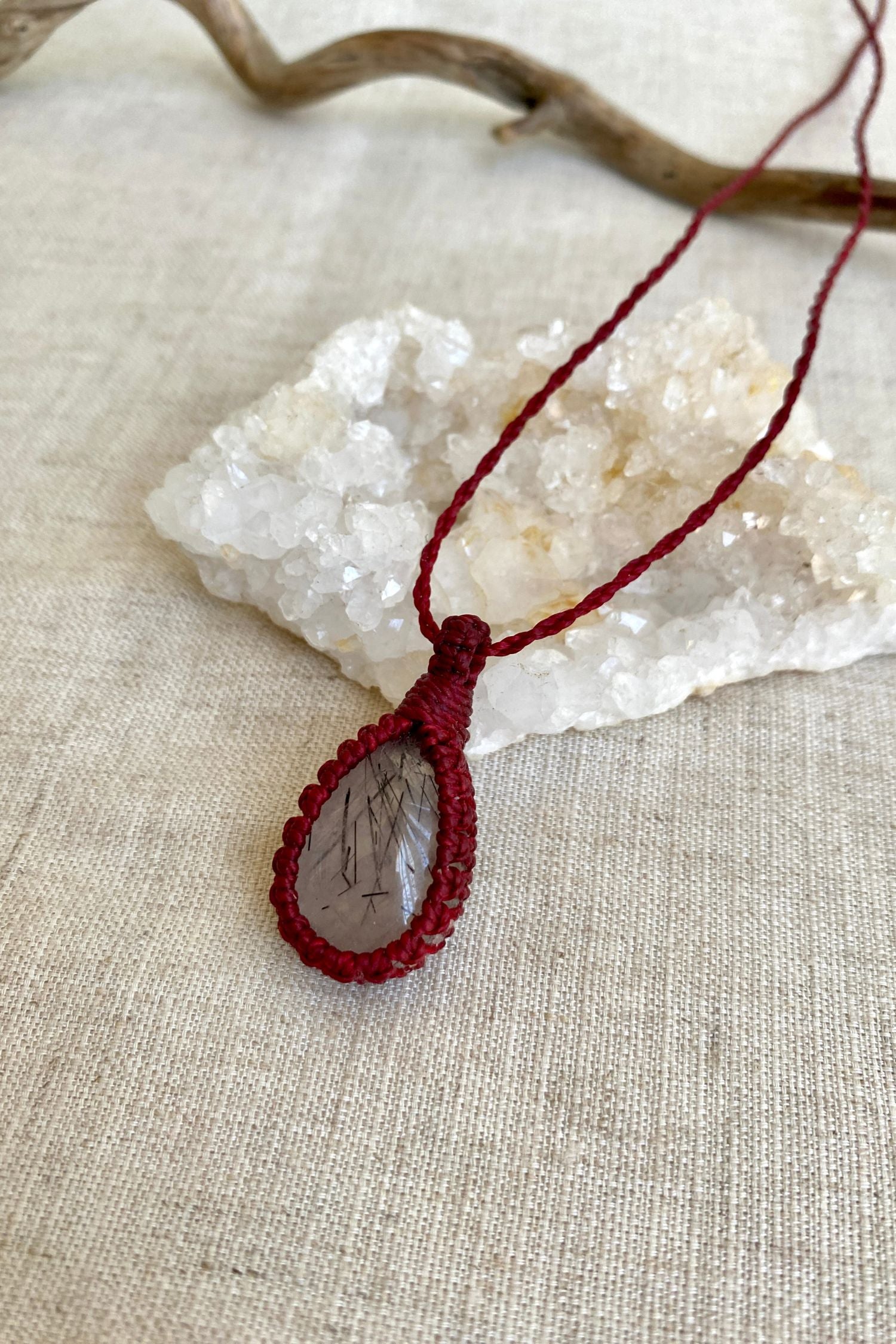 Side-angle view of a handmade Tourmaline Quartz macrame necklace, showcasing the red macrame cord and the gemstone’s unique inclusions.