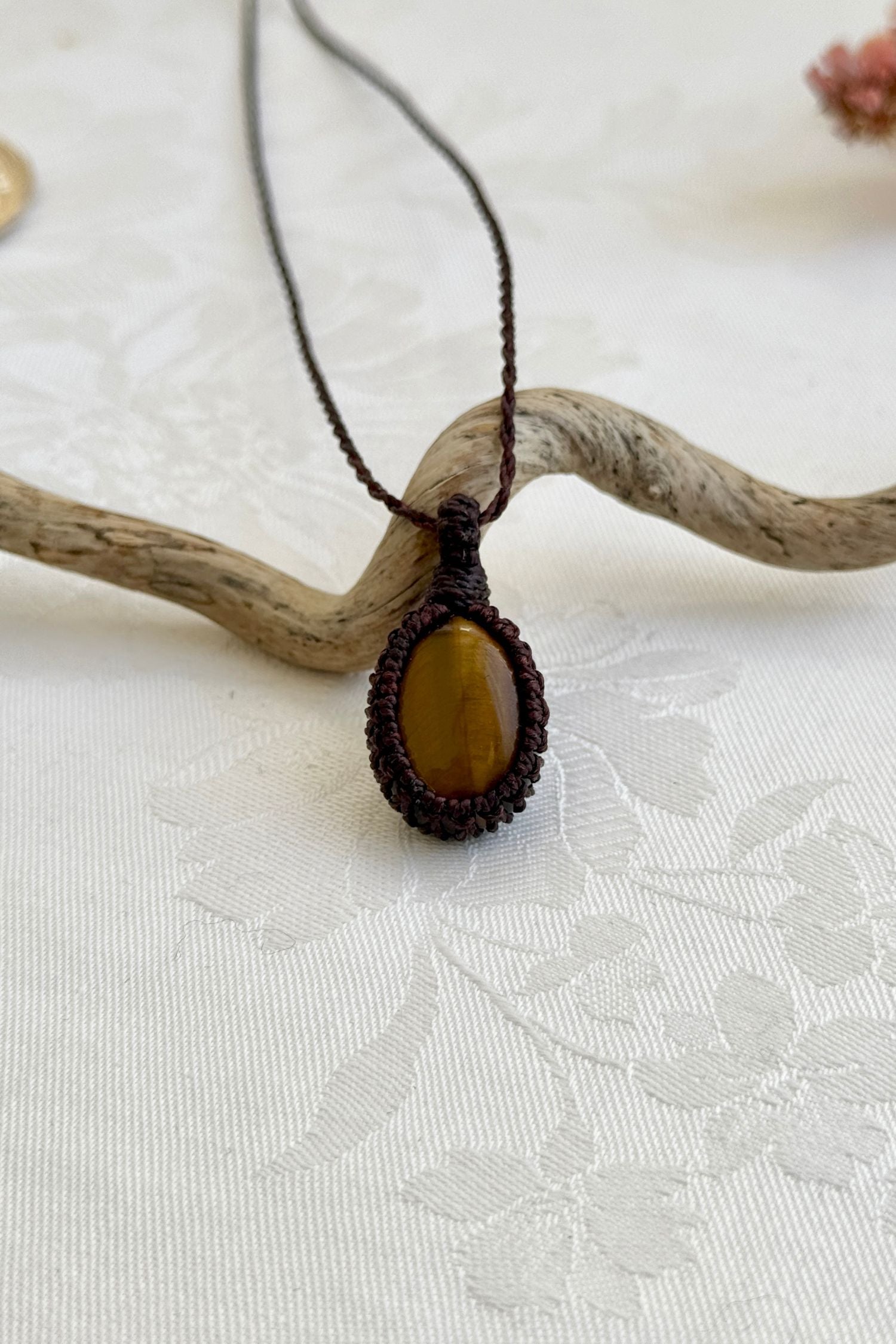 Handmade Tiger’s Eye macrame necklace with a brown cord, laid flat to display its intricate design and glowing gemstone.