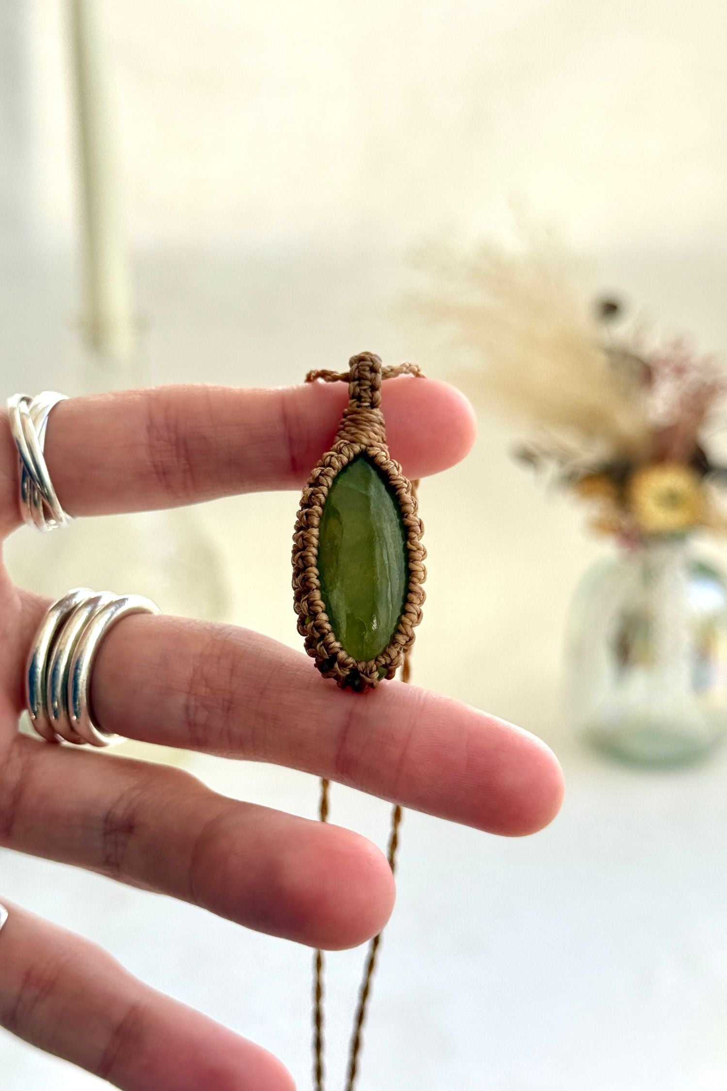 Hand holding a handmade rare Vesuvianite macrame necklace with a golden brown cord, showcasing the gemstone's soft, subtle green hue.
