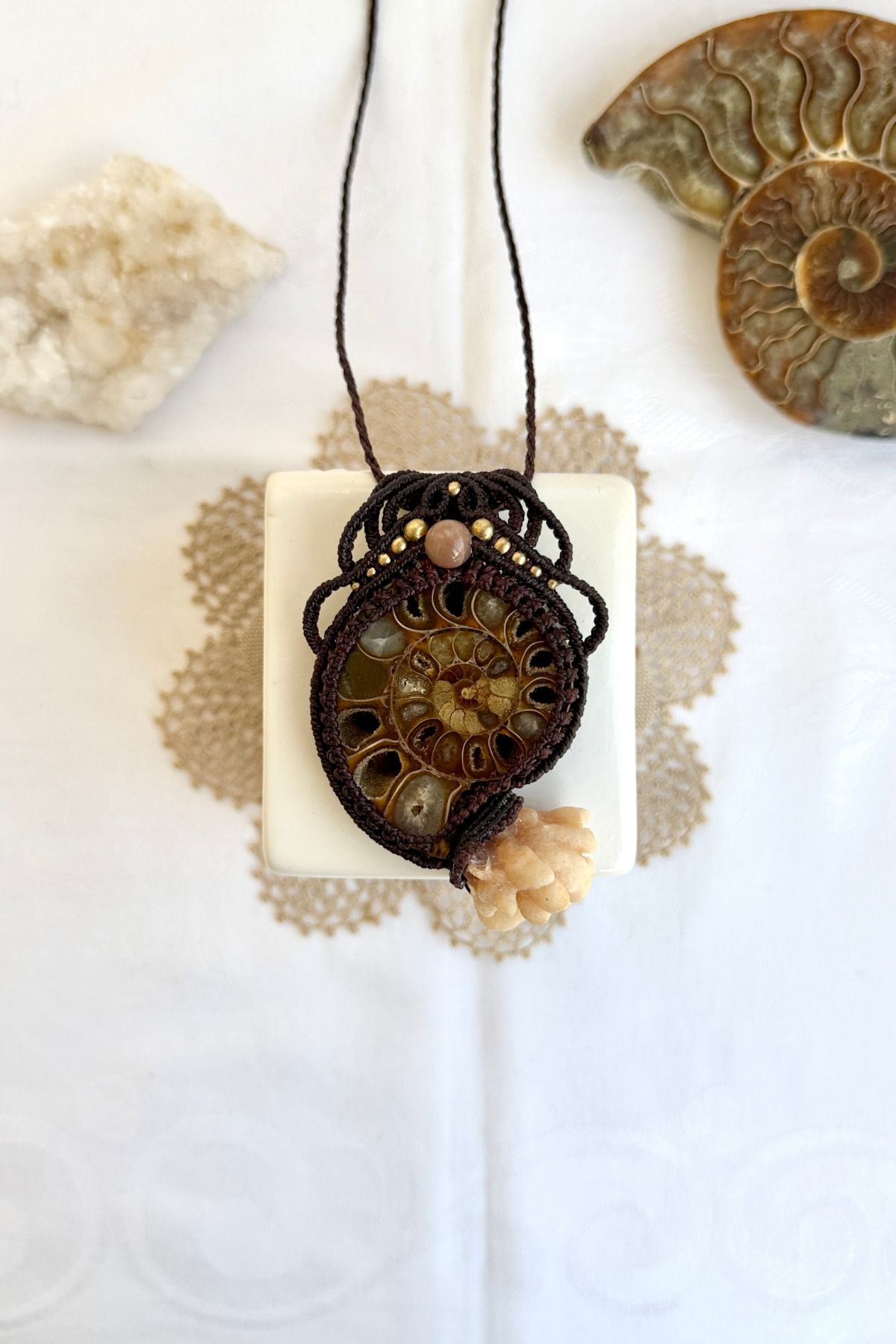 Large ammonite fossil pendant necklace with coral-like calcite tendrils and peach moonstone laid flat on light background