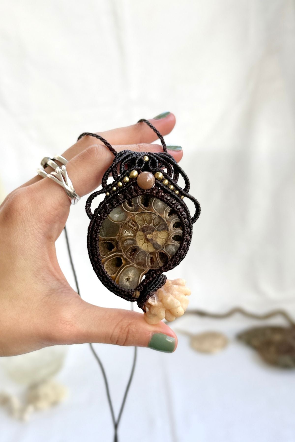 Hand holding one of a kind ammonite fossil necklace with calcite coraloid tentacles, showing scale and artisan detail