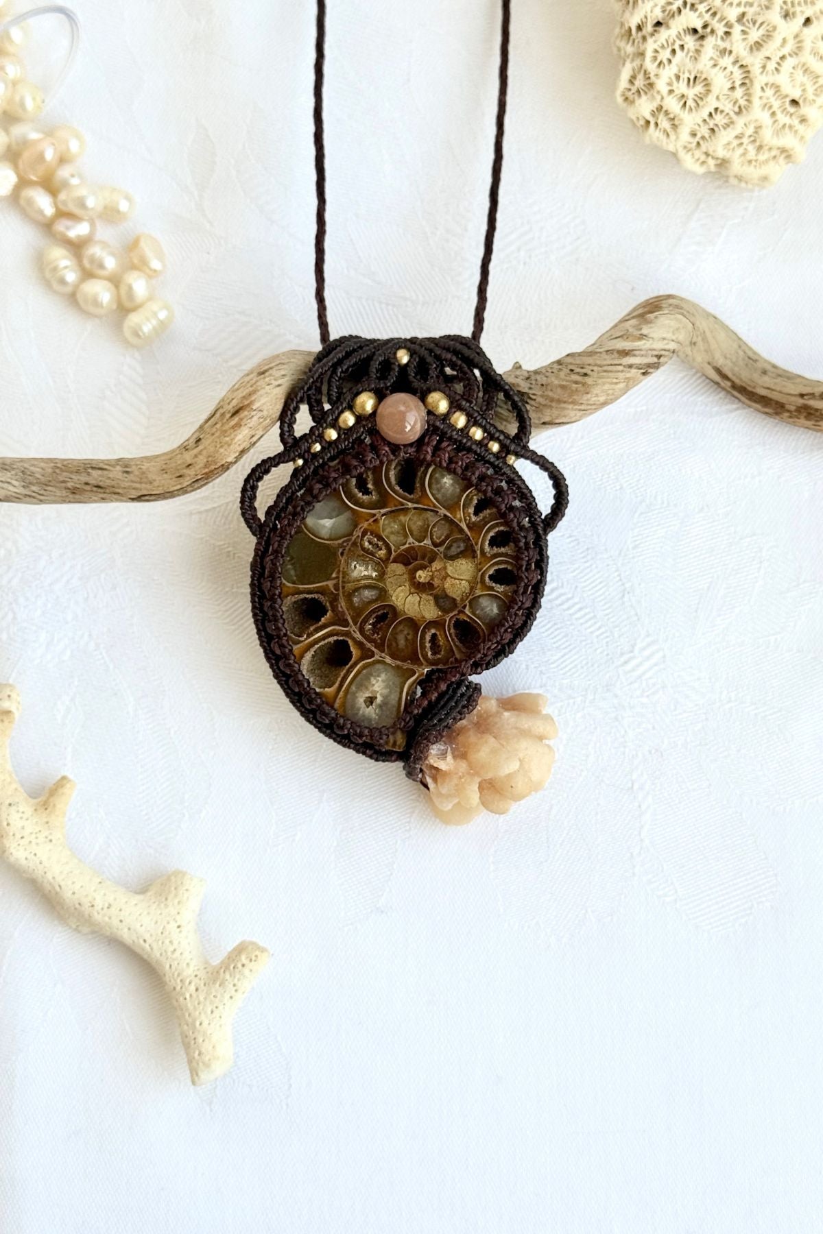 Ammonite fossil pendant necklace with calcite coraloid “tentacles”, peach moonstone and freshwater pearls displayed in ocean inspired styled scene