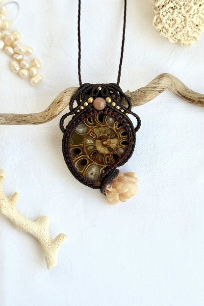 Ammonite fossil pendant necklace with calcite coraloid “tentacles”, peach moonstone and freshwater pearls displayed in ocean inspired styled scene