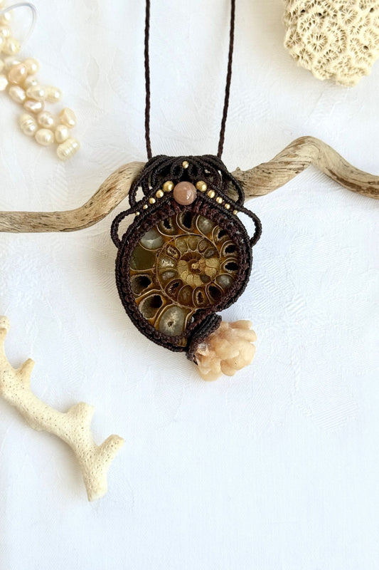 Ammonite fossil pendant necklace with calcite coraloid “tentacles”, peach moonstone and freshwater pearls displayed in ocean inspired styled scene