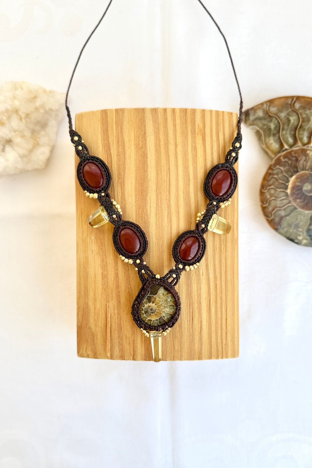 V-shaped ammonite necklace laid flat in styled scene with vivid carnelian stones and smoky quartz points, elegant ocean inspired design