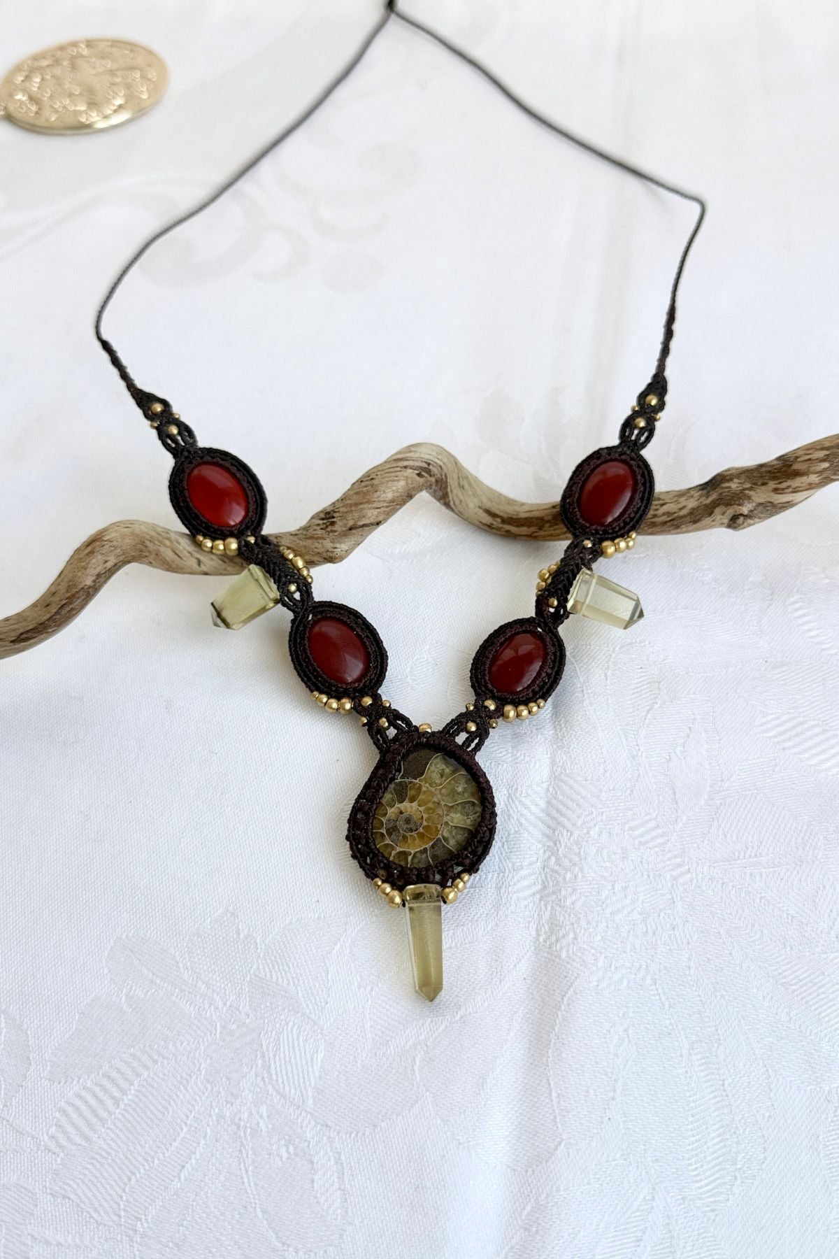 V-shaped ammonite necklace laid flat on simple background highlighting central ammonite, carnelian accents, smoky quartz points, and cord design