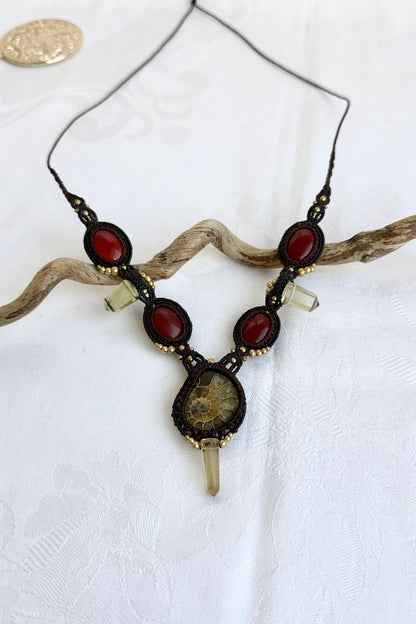 V-shaped ammonite necklace laid flat on simple background highlighting central ammonite, carnelian accents, smoky quartz points, and cord design