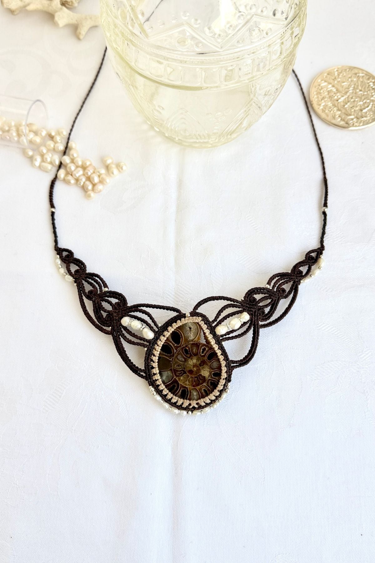 Large ammonite fossil statement necklace with freshwater pearls and coral accents displayed in an ocean inspired styled scene