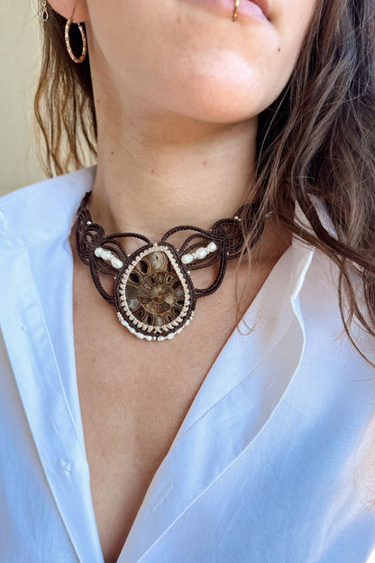 Model wearing one of a kind ammonite fossil statement necklace in V-shaped silhouette with freshwater pearls, styled elegantly