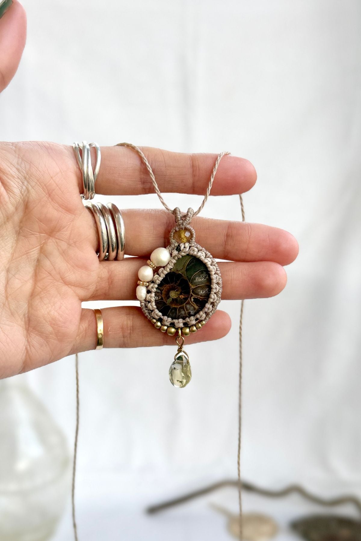 Hand holding ammonite fossil necklace with freshwater pearls, rutilated quartz accent and lemon quartz drop showing natural details