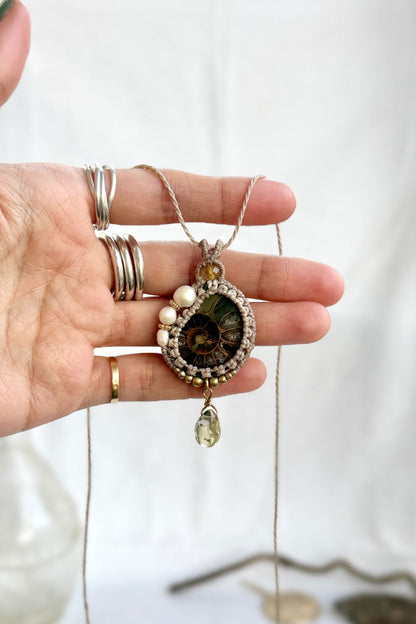 Hand holding ammonite fossil necklace with freshwater pearls, rutilated quartz accent and lemon quartz drop showing natural details