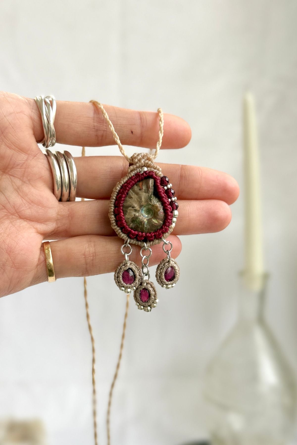 Ammonite fossil and garnet drop necklace shown in hand, refined ocean inspired jewelry