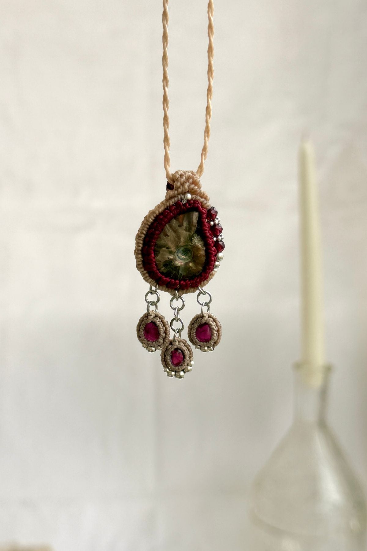 Backlit garnet drop necklace with natural ammonite fossil, showcasing translucent wine red gemstones