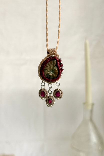 Backlit garnet drop necklace with natural ammonite fossil, showcasing translucent wine red gemstones