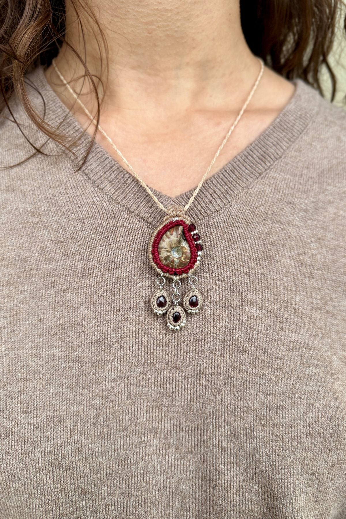 Model wearing delicate ammonite fossil and garnet drop necklace, elegant statement jewelry